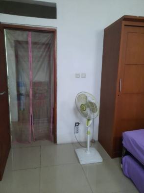 Sudut kamar dengan lemari kayu, kipas berdiri, dan pintu di Kos Muslimah Bukit Azikra